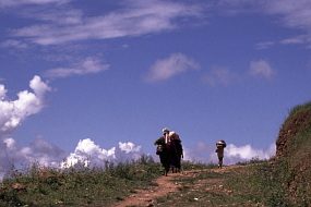 大きなカゴを背負って山道をゆく人々。空と雲のコントラストがくっきり。