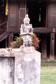 仏像がちょこんと載った門柱の奥には高床式の住宅。
